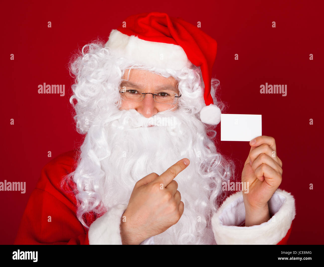 Portrait of a santa holding blank visiting card over red background ...