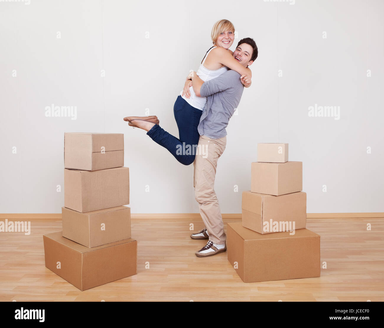 Happy young couple in a close ecstatic embrace smiling happily as they stand surrounded by cartons in their new home Stock Photo