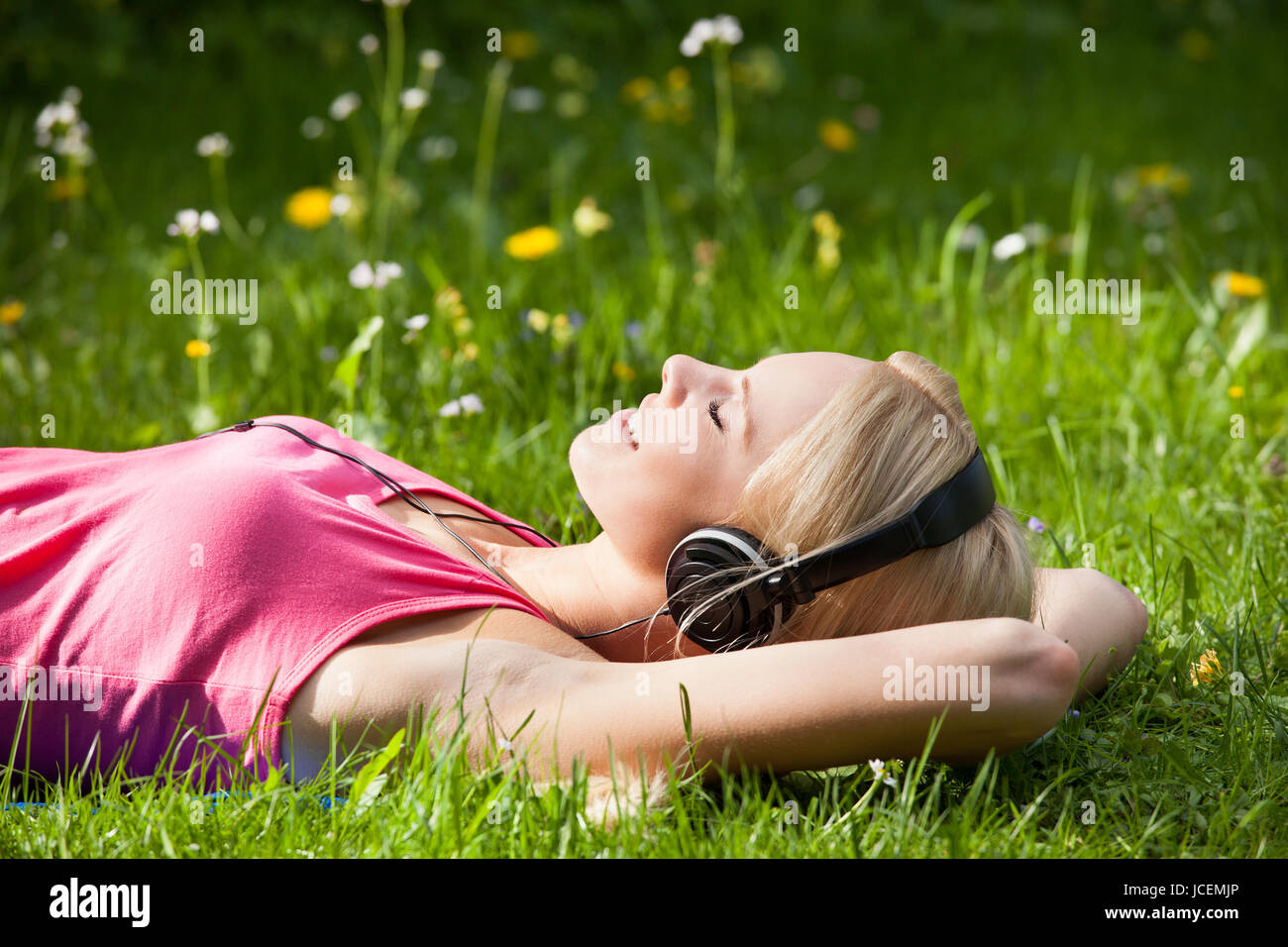 Portrait Of Young Woman Lying On Grass And Listening To Music With ...