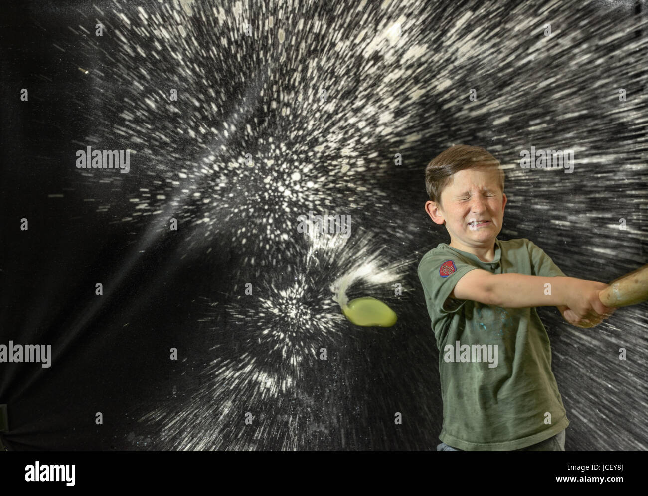 Young boy, eyes closed, and with a look of determination on his face, smashes a water balloon with a bat Stock Photo