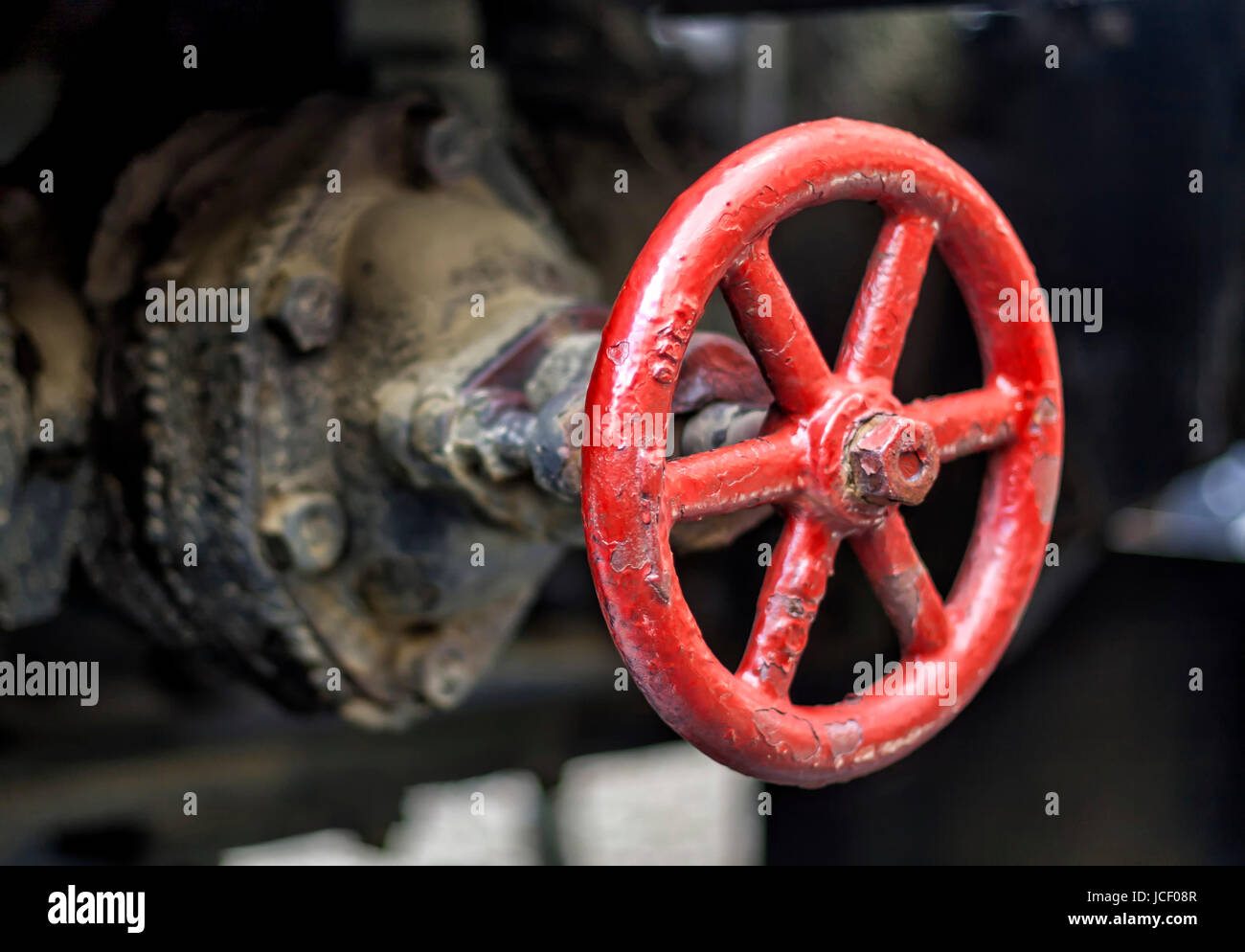 A grimmy red wheel valve regulating the flow of industial base liquids. Stock Photo