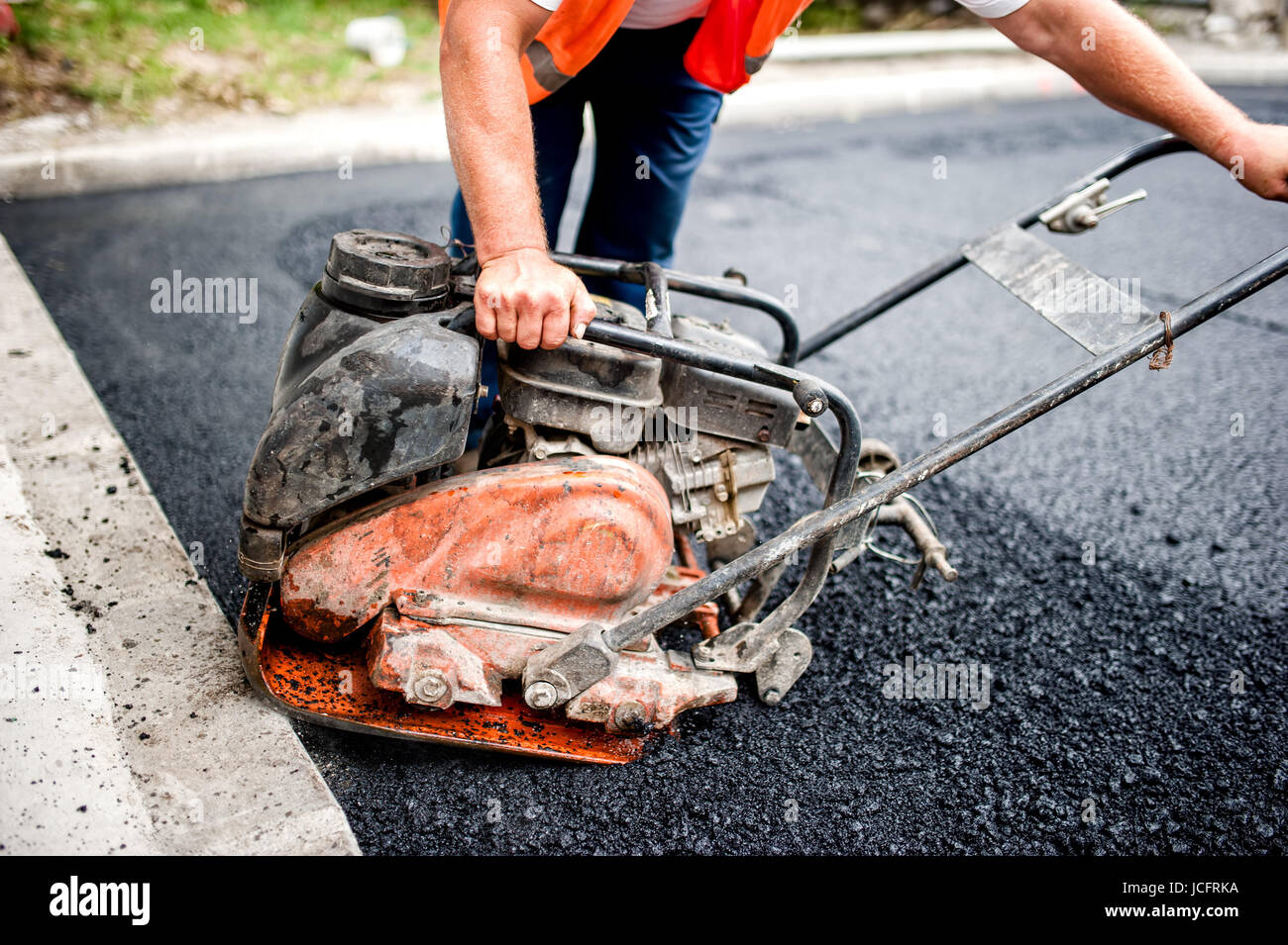 asphalt worker at road construction site with compactor plate and tools ...