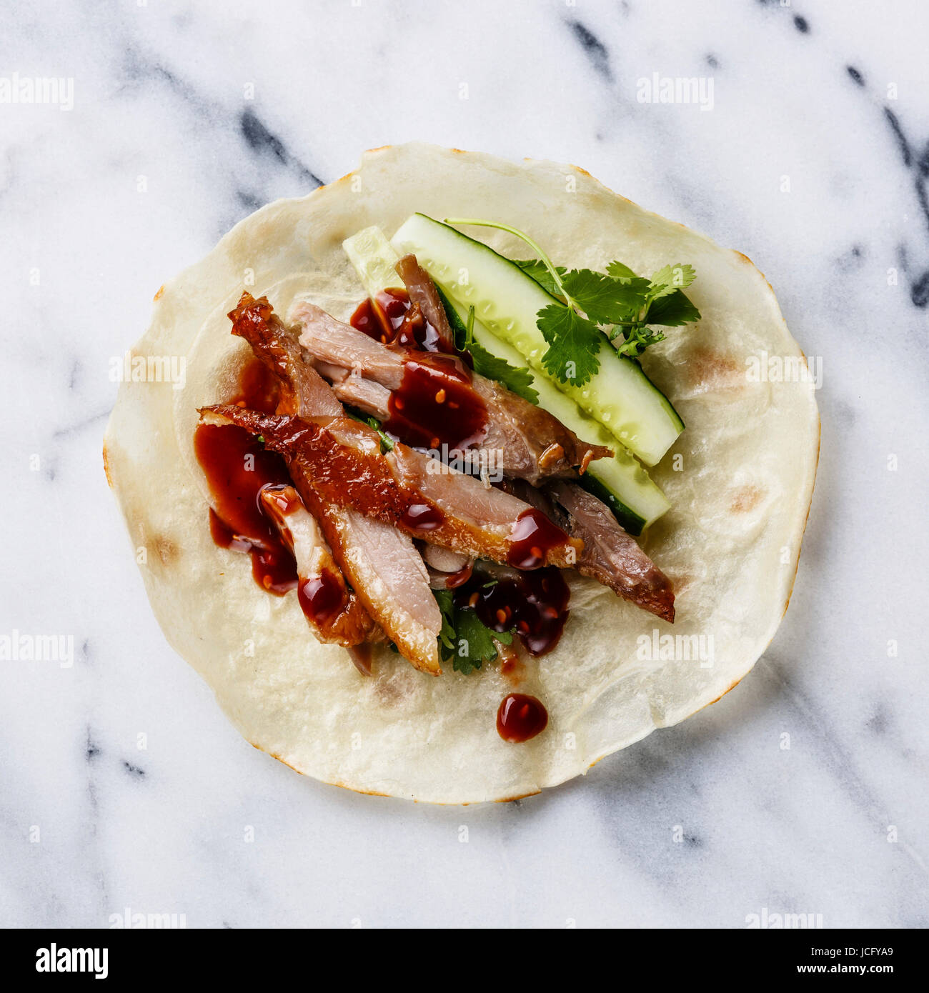 Peking Duck with cucumber, green onions and cilantro in roasted wheaten chinese pancakes with sauce close-up serving size on marble background Stock Photo