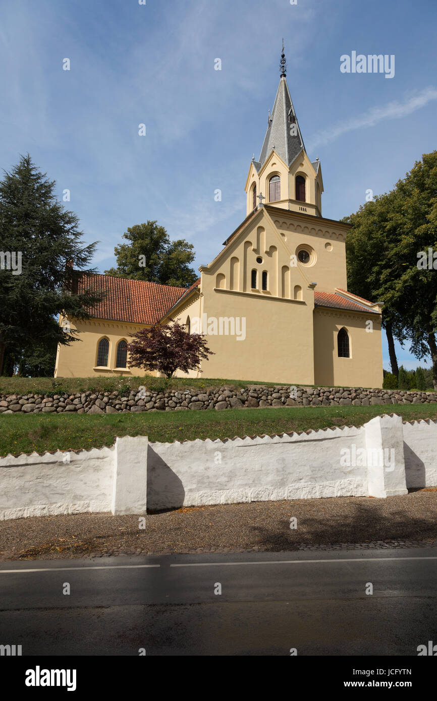 Gelbe Kirche hinter weißer Friedhofsmauer Stock Photo