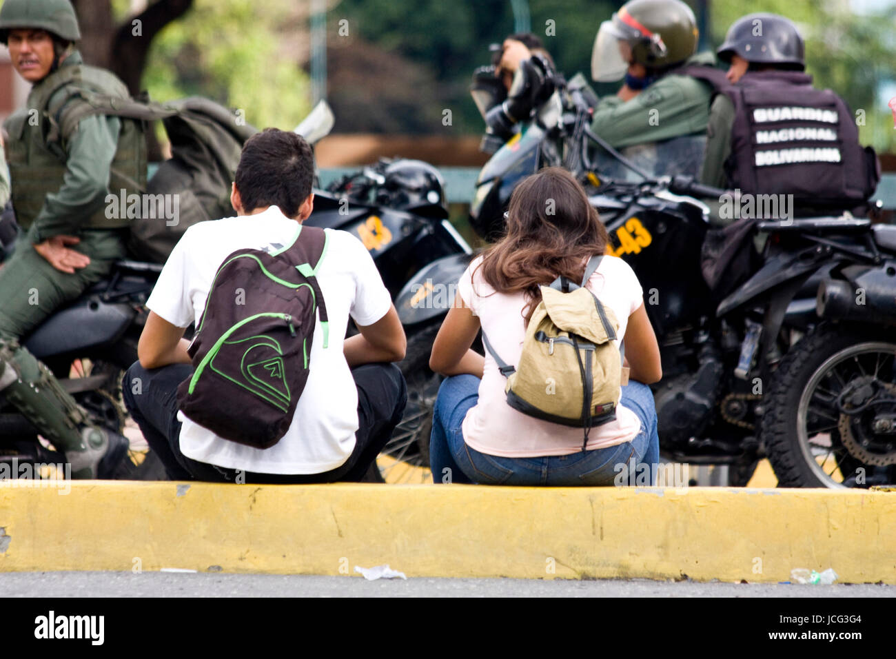 Two protesters sit in front of a group of Bolivarian National Guards during a protest in Caracas against the government of Nicolas Maduro. Stock Photo