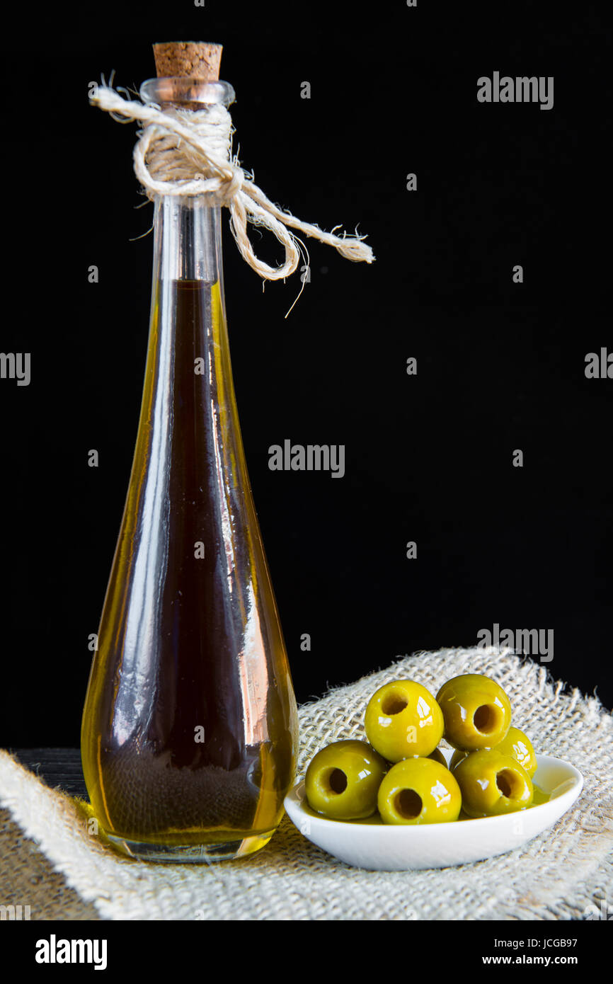 Extra virgin olive oil and pitted green olives on a black background ...
