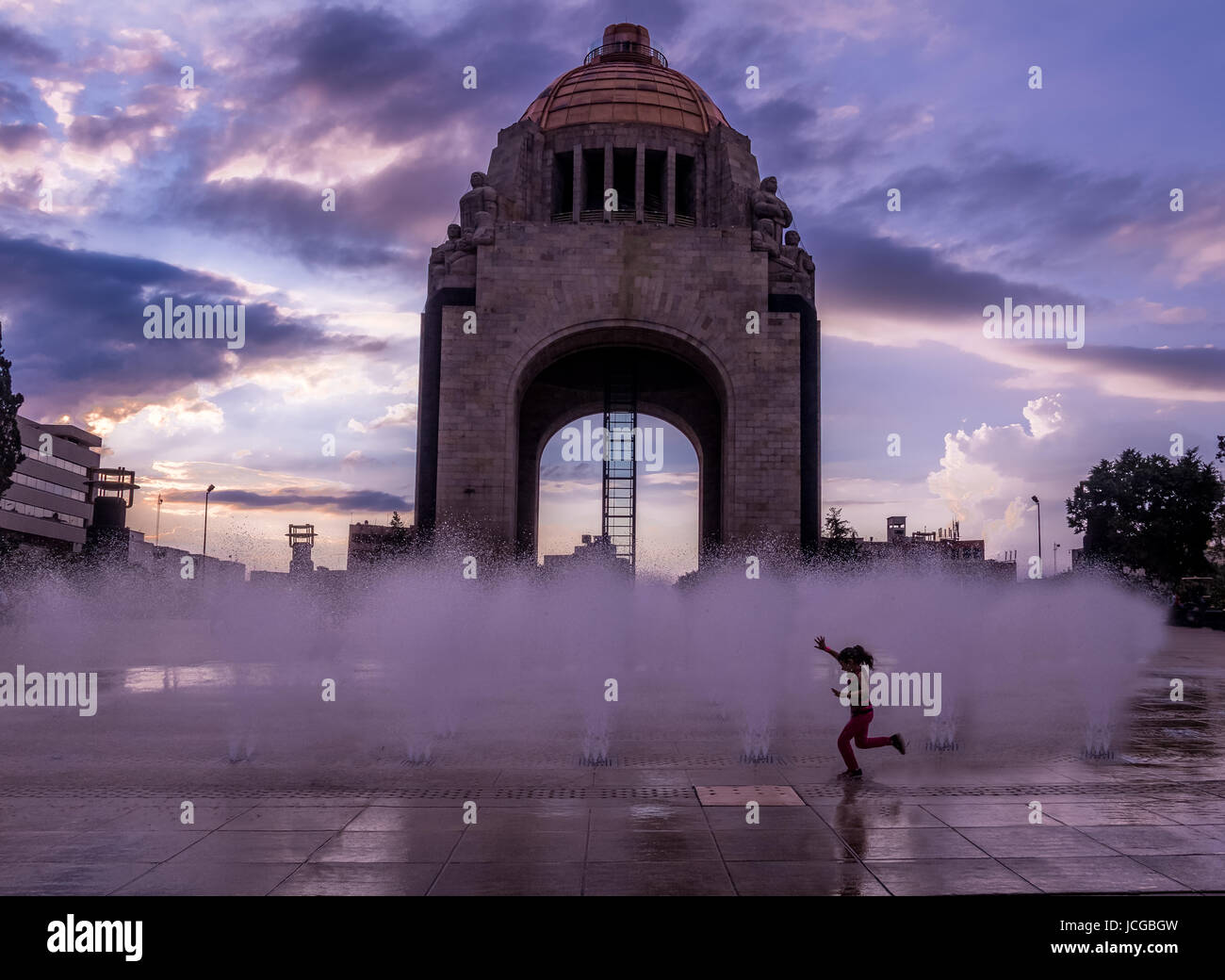 Girl playing with the water fountain in front of Monument to the Mexican Revolution (Monumento a la Revolucion) - Mexico City, Mexico Stock Photo