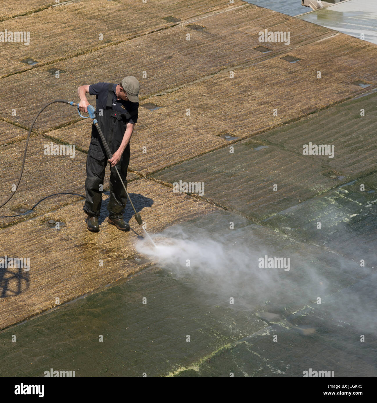 Man using a waterjet to clean green algae from a concrete marina