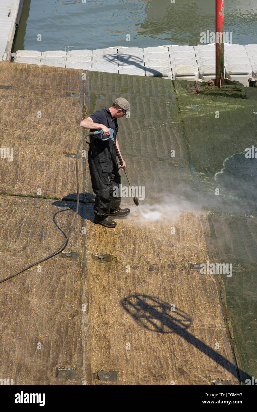 Man using a waterjet to clean green algae from a concrete marina