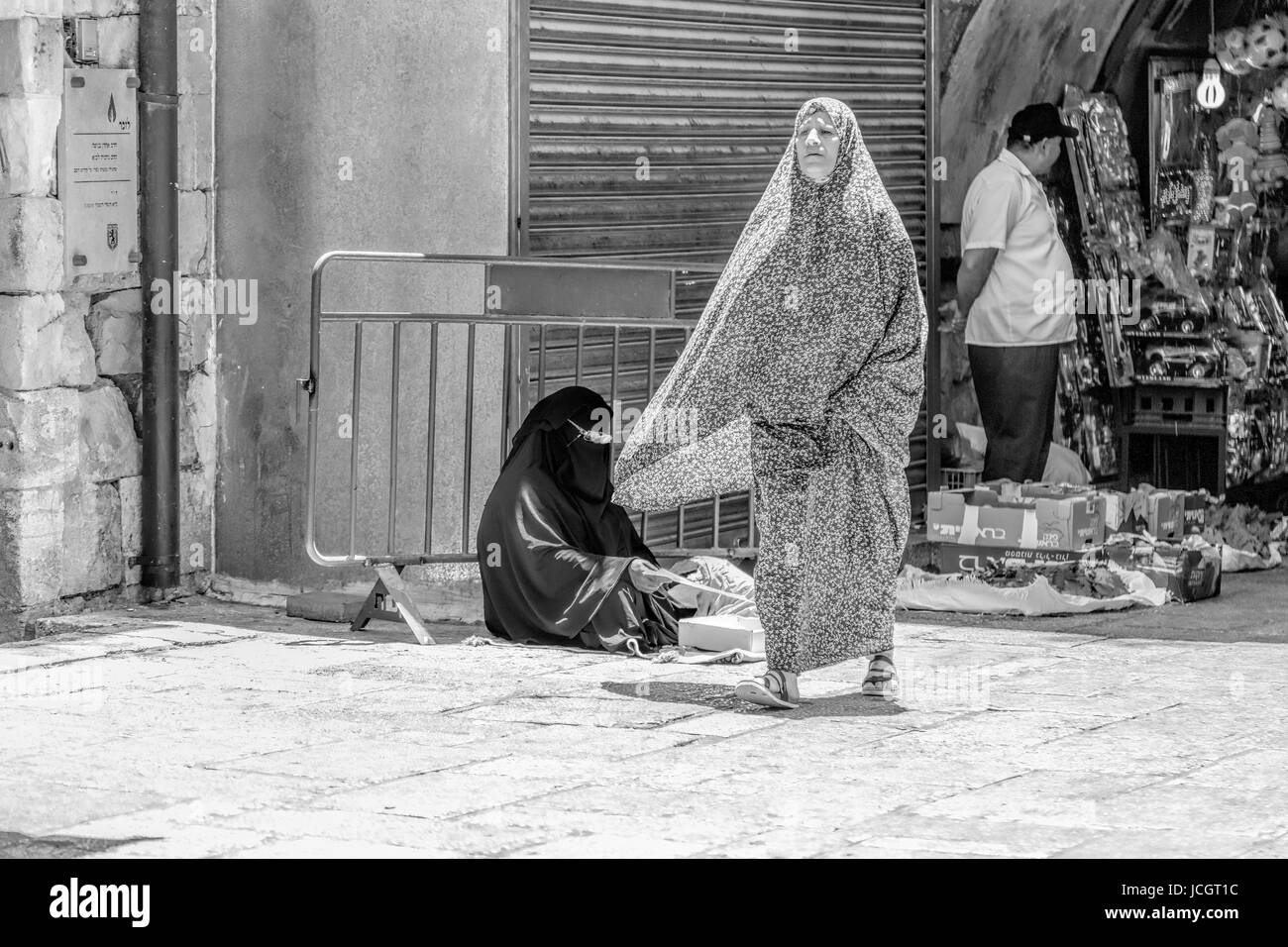Seated woman with a NIQAB, a face veil and a walking woman in a CHADOR, a traditional Muslem dress in the Arab Quarter,Old City of Jerusalem, Israel. Stock Photo