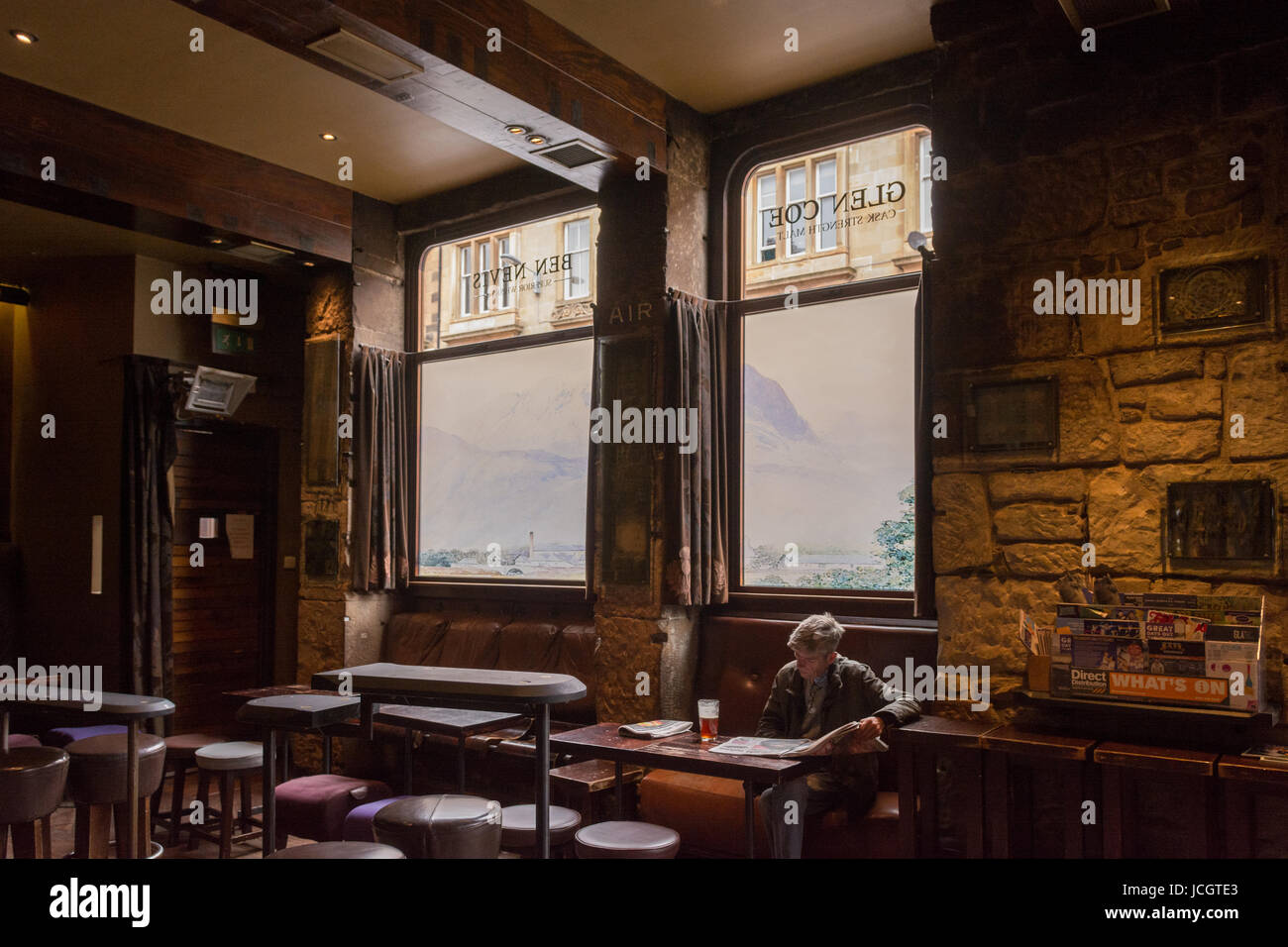 The Ben Nevis pub, Finnieston, Glasgow, Scotland - man drinking pint and reading newspaper in front of Ben Nevis scene painted on windows Stock Photo