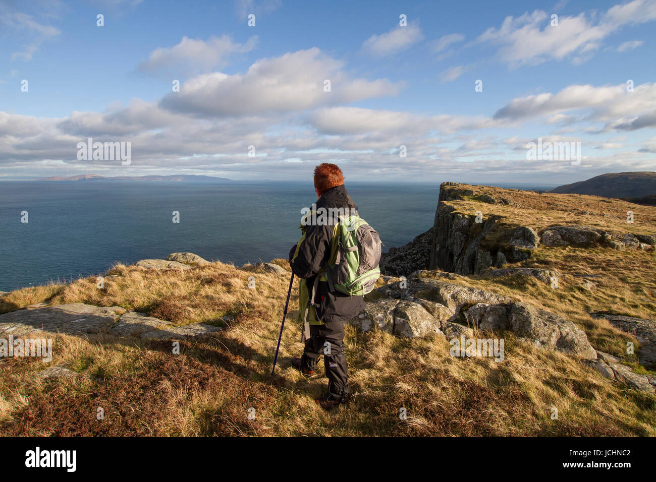 A hill-walker looks out to sea from the cliff-top walk at Fair Head, Ballycastle,County Antrim, Northern Ireland. Stock Photo