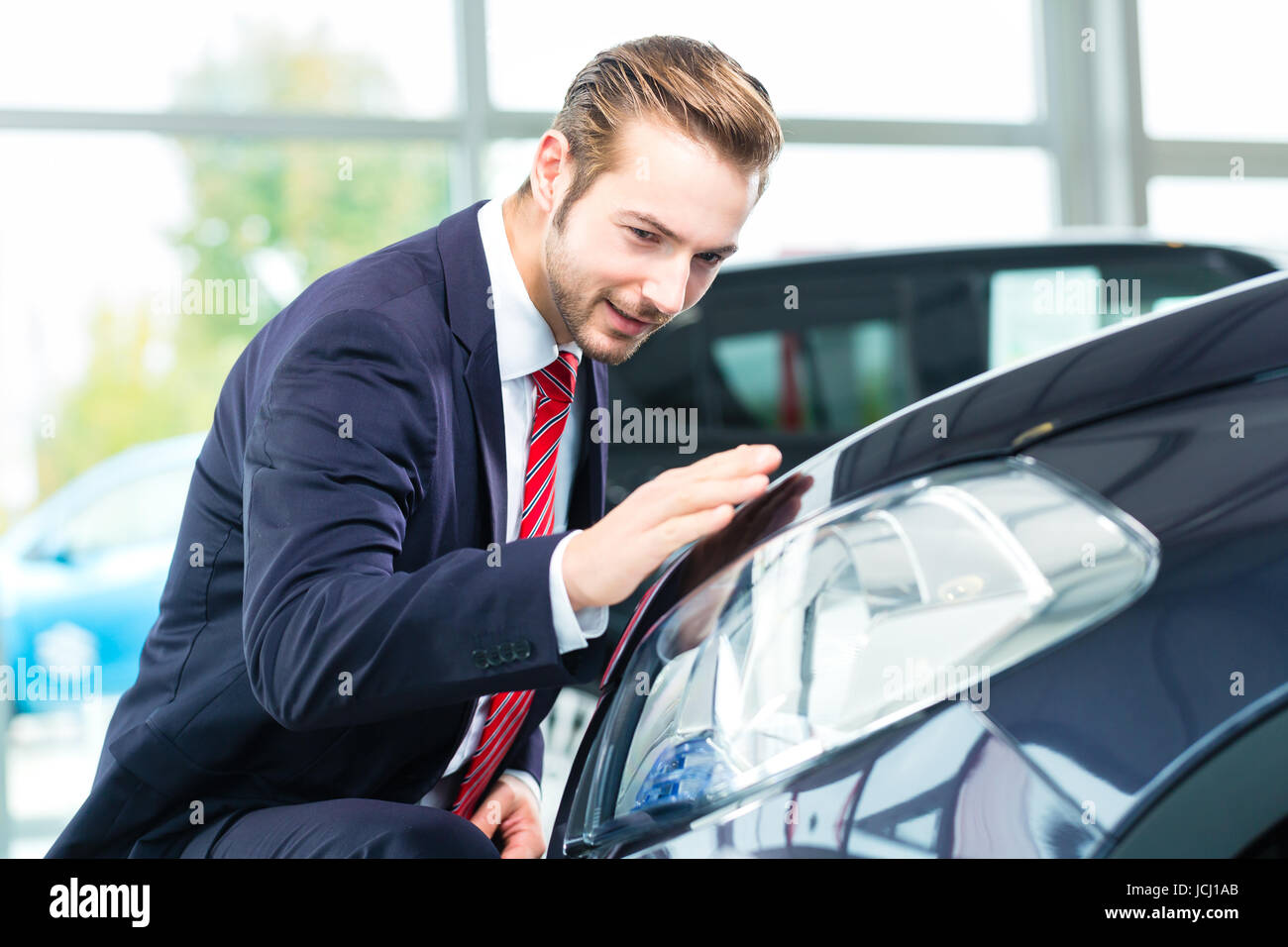Seller or car salesman in car dealership presenting the reflecting car