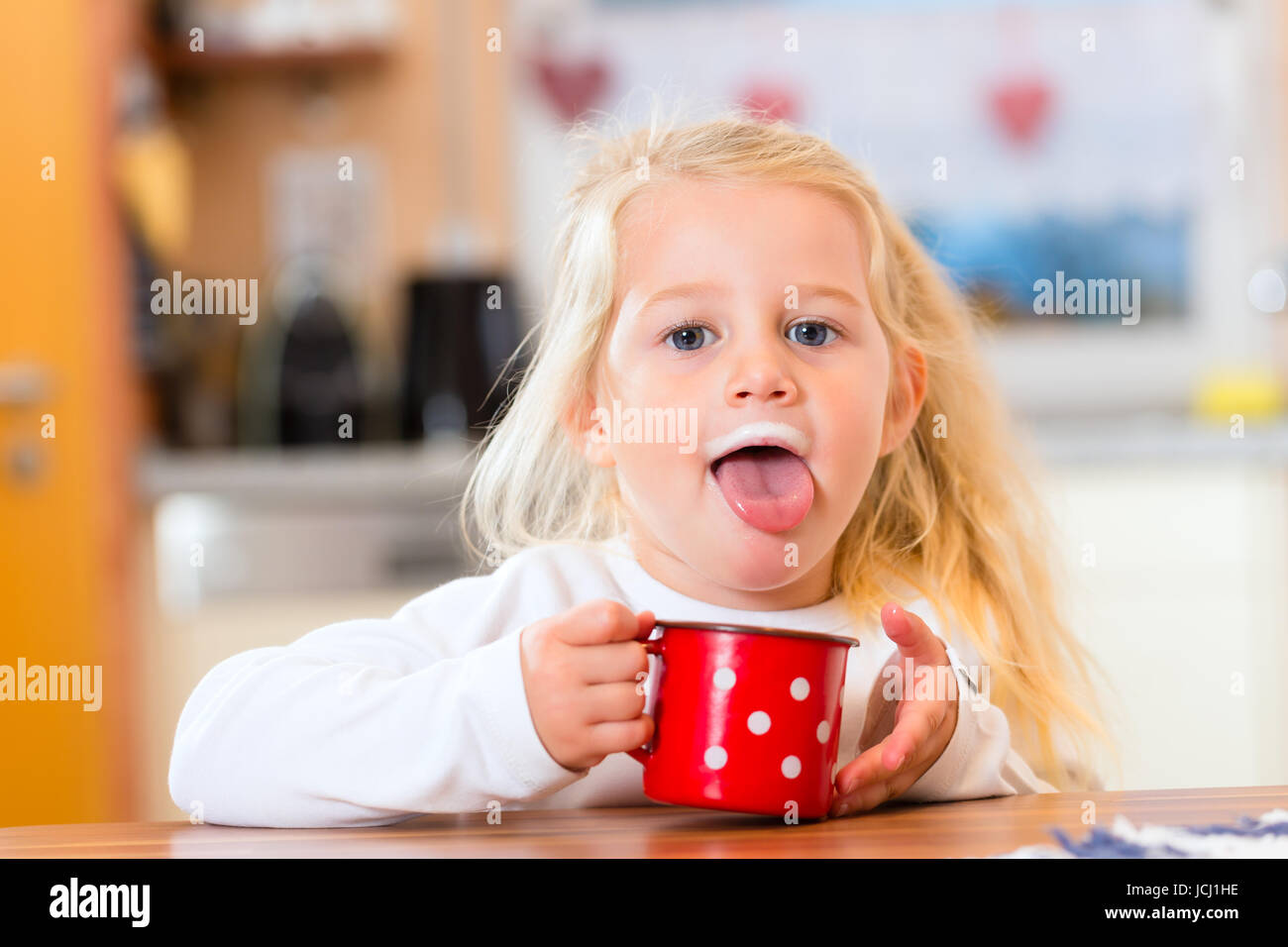 child drinking cup or mug of milk in the domestic kitchen Stock