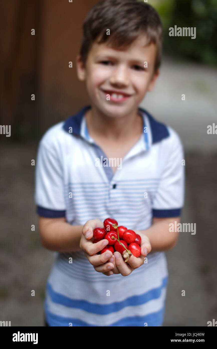 Happy little caucasian boy holding cherries in hands outdoor Stock Photo