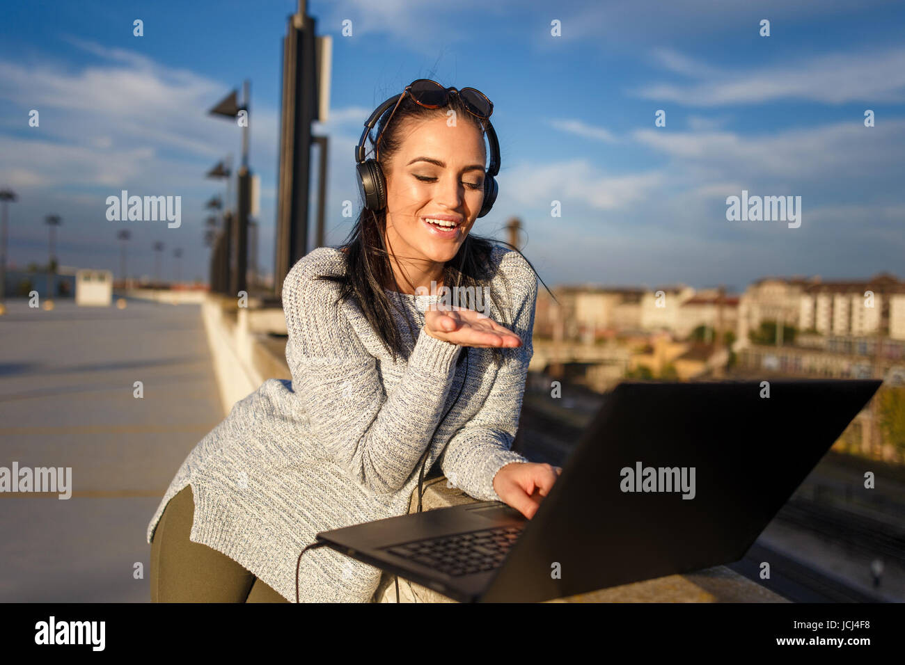Happy young caucasian woman sending kiss online by laptop outdoor Stock Photo