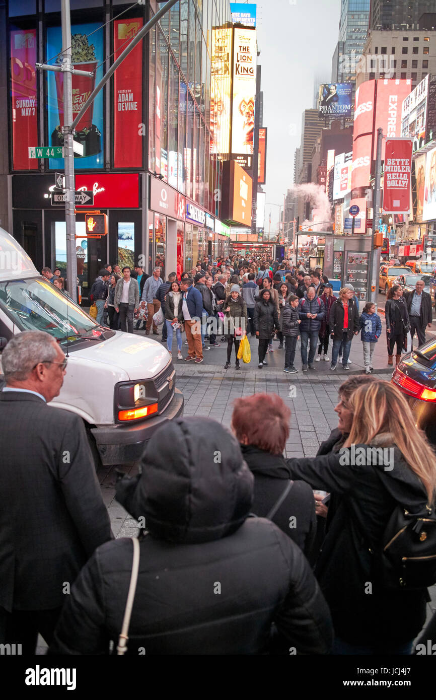 people waiting at crosswalk with full busy sidewalk in the evening evening in Times Square New York City USA Stock Photo