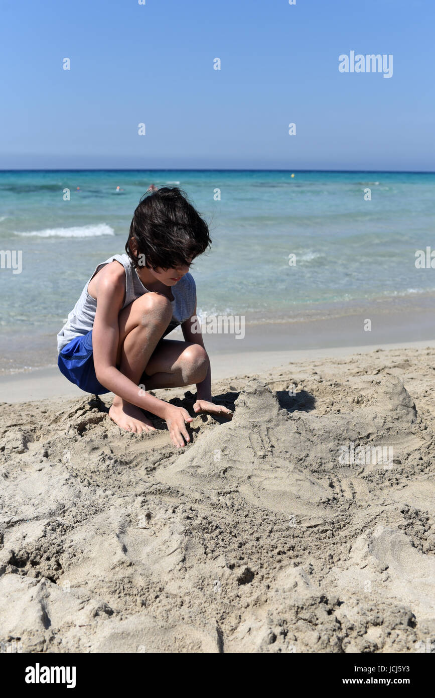Boy sand sculpting on a sandy beach, Menorca, Spain Stock Photo