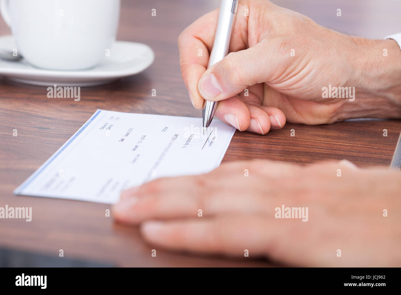 Male Hand Filling Out The Amount On A Cheque Stock Photo