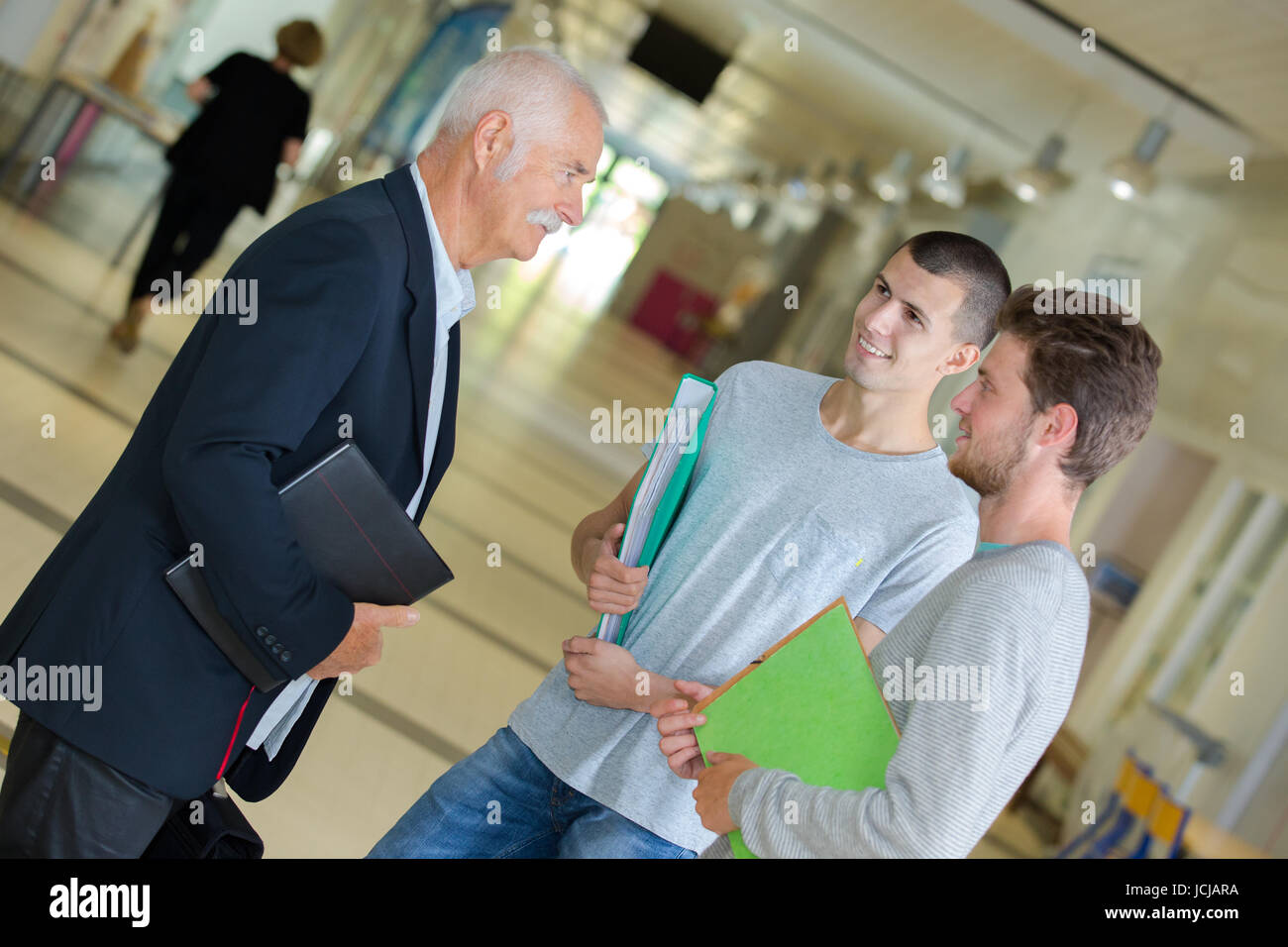high school teacher talking to students in corridor Stock Photo