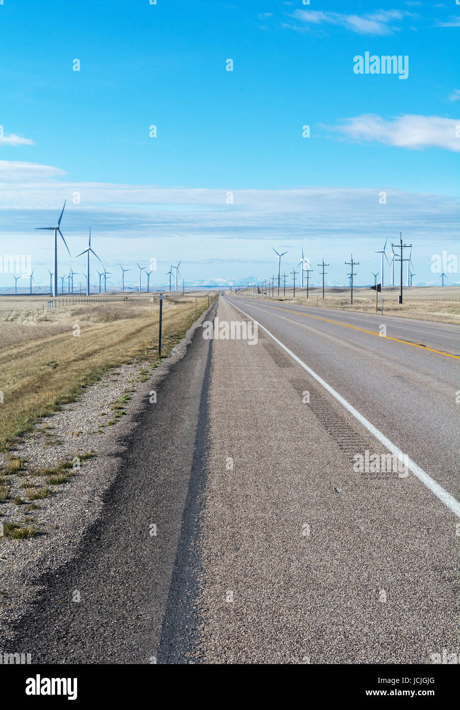 A wind swept pairie cut by a orad and dotted with wind turbines Stock