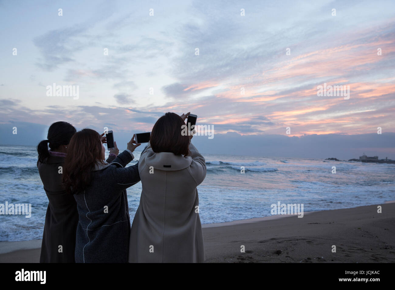 Back of three middle aged women taking selfie on beach at sunrise Stock Photo