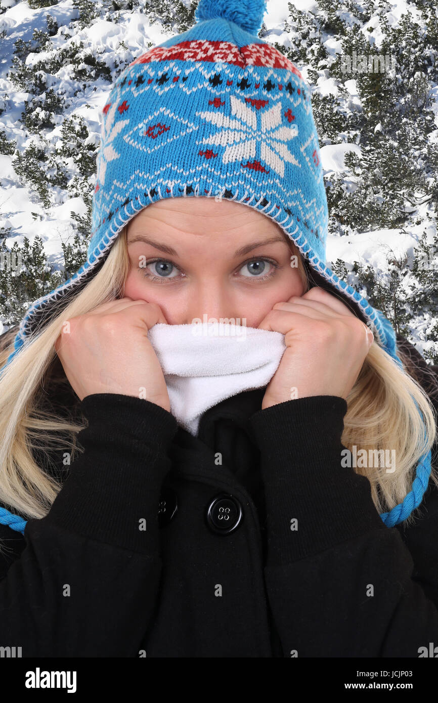 Junge Frau im Winter beim Frieren in der Kälte mit Mütze im Wald Stock Photo