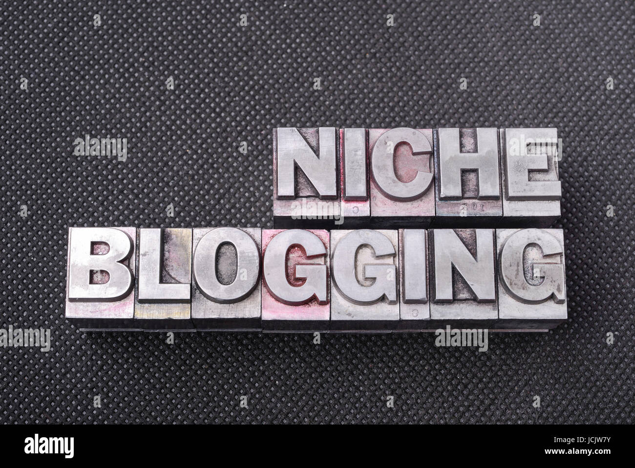 niche blogging phrase made from metallic letterpress blocks on black perforated surface Stock Photo