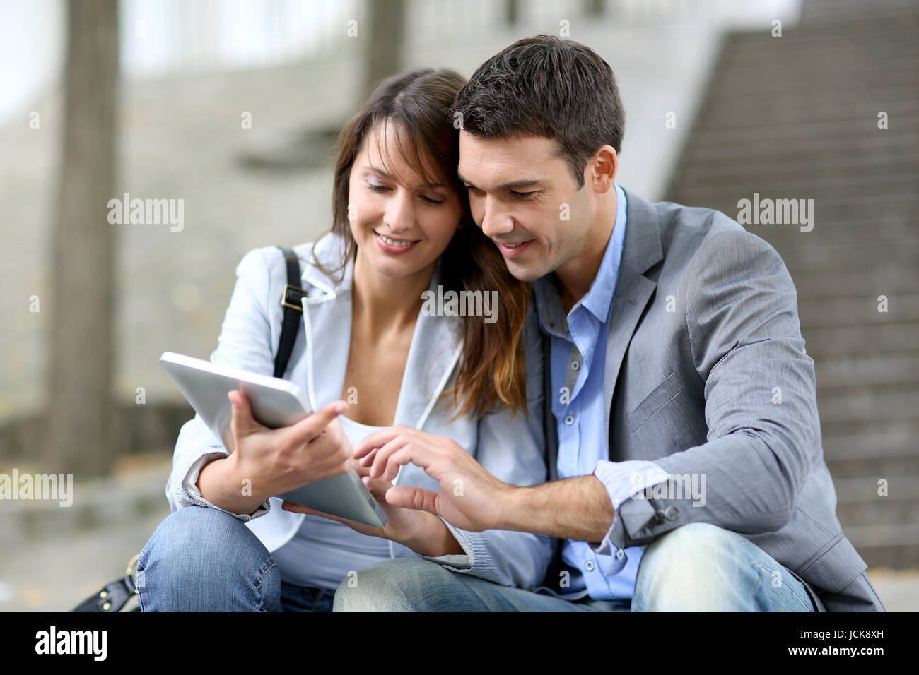 Cheerful couple sitting in stairs with electronic tablet Stock Photo