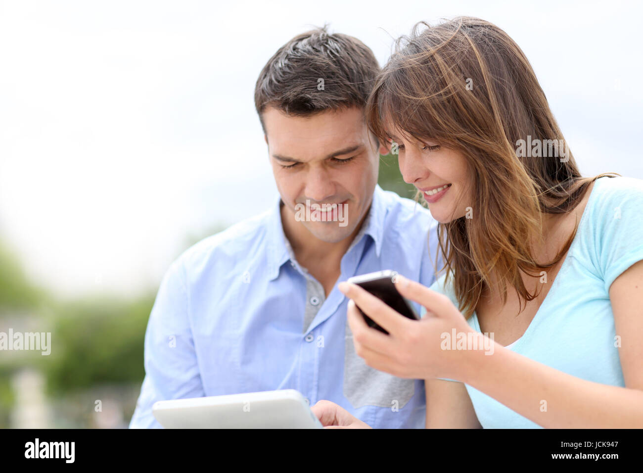 Couple using tablet and cellphone in public park Stock Photo