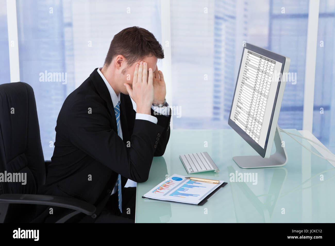 Young businessman suffering from headache at computer desk in office Stock Photo