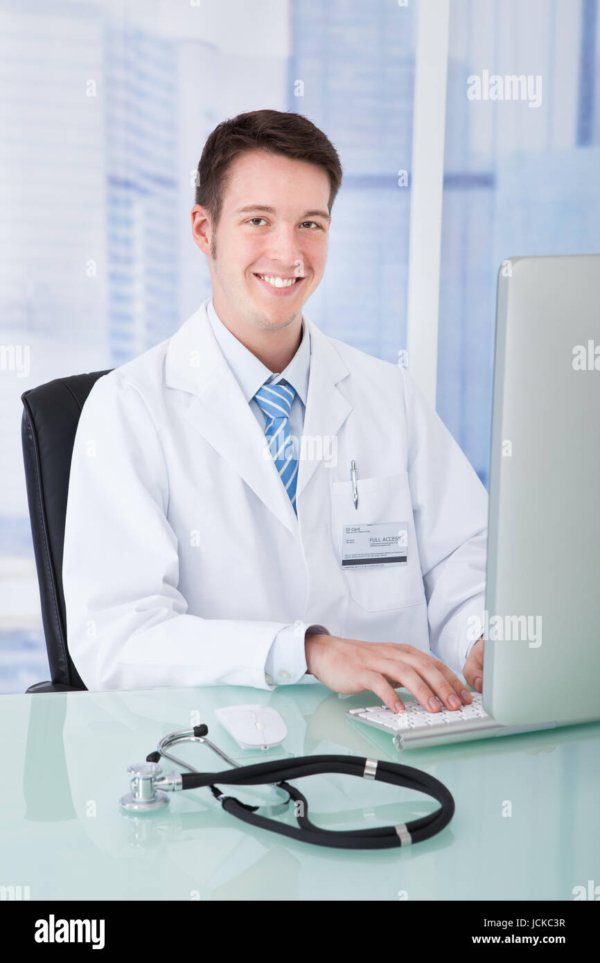Portrait of confident young male doctor using computer at desk in ...
