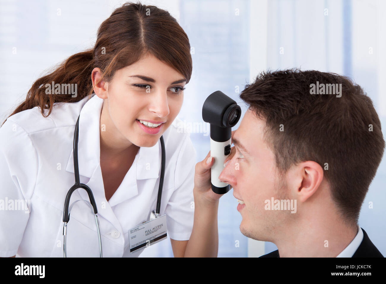 Young female doctor examining businessman's forehead with dermoscope in clinic Stock Photo