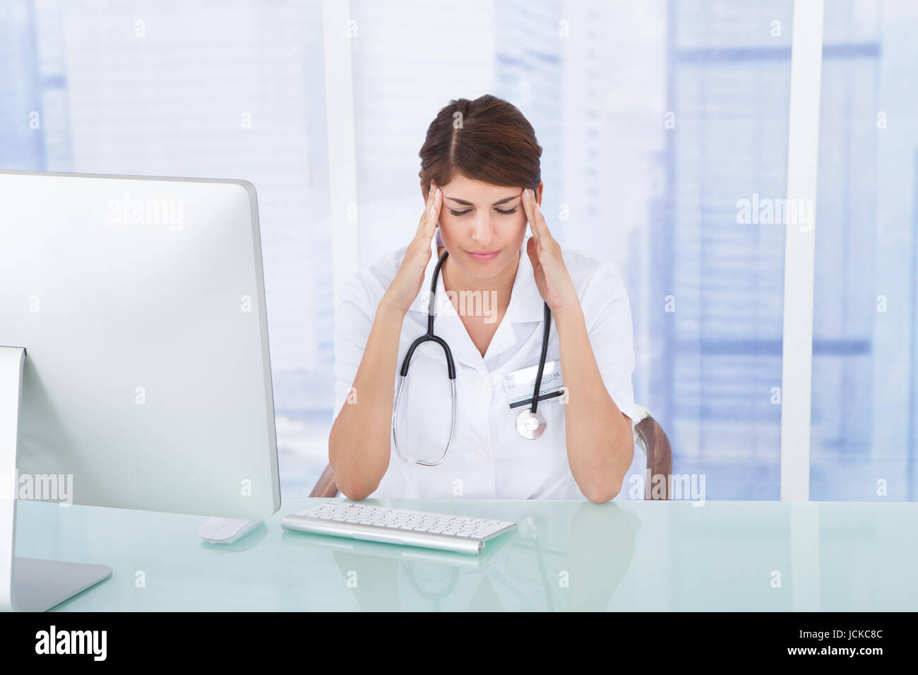Sad female doctor with headache at computer desk in clinic Stock Photo ...