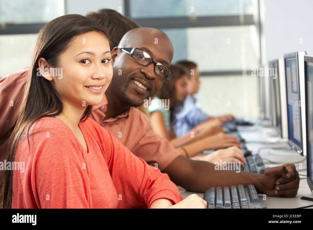 Teacher Helping Students Working At Computers In Classroom Stock Photo ...