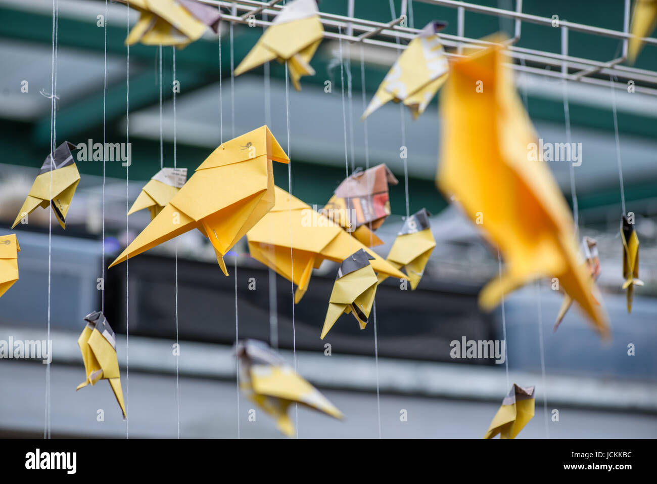 Origami yellow orange paper cranes birds hanging over industrial architectural blurred background Stock Photo
