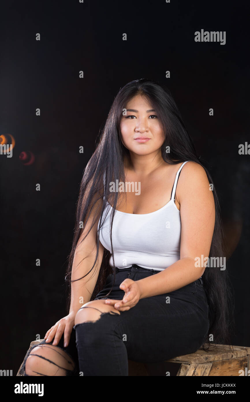 Beautiful curvy girl with dark hair and cheerful personality in a white  t-shirt on a dark background Stock Photo - Alamy