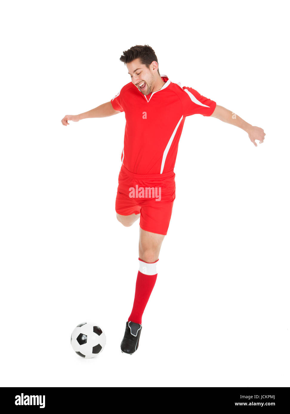 Full length of young soccer player kicking football over white