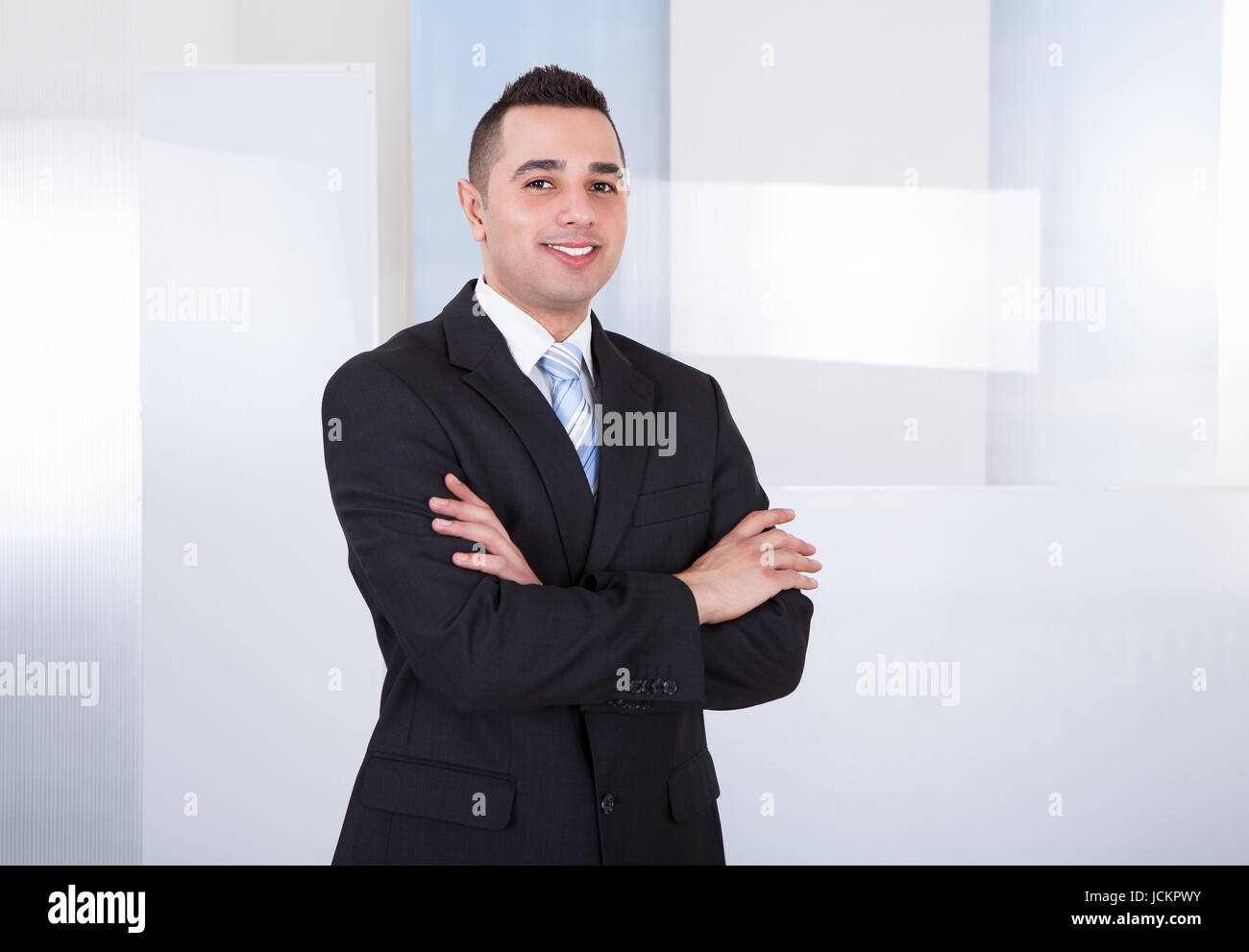 Portrait of handsome young businessman standing arms crossed in office ...