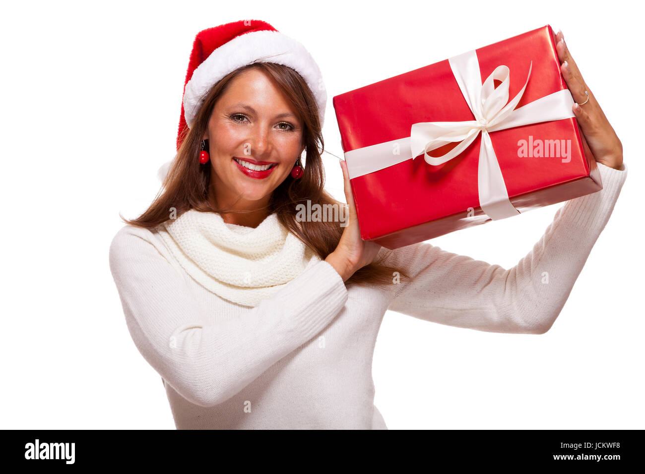 Hübsche brünette Frau mit Weihnachtsmütze und großem roten Geschenk fröhlich lachend isoliert vor weißem Hintergrund Stock Photo