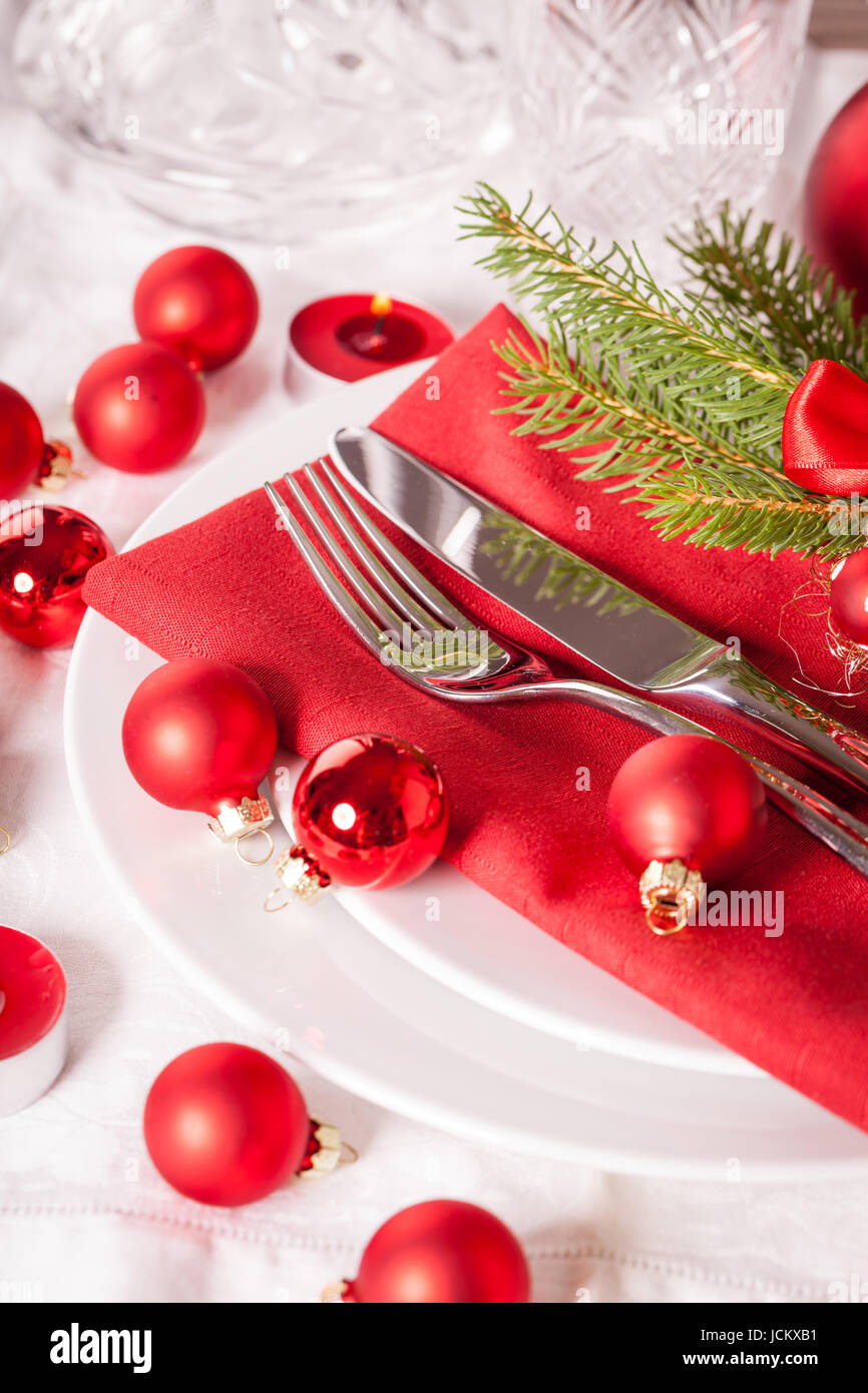 Rote Serviette mit weihnachtlichen Glaskugeln und Besteck mit einem grünen Tannenzweig und roter Schleife Nahaufnahme Stock Photo