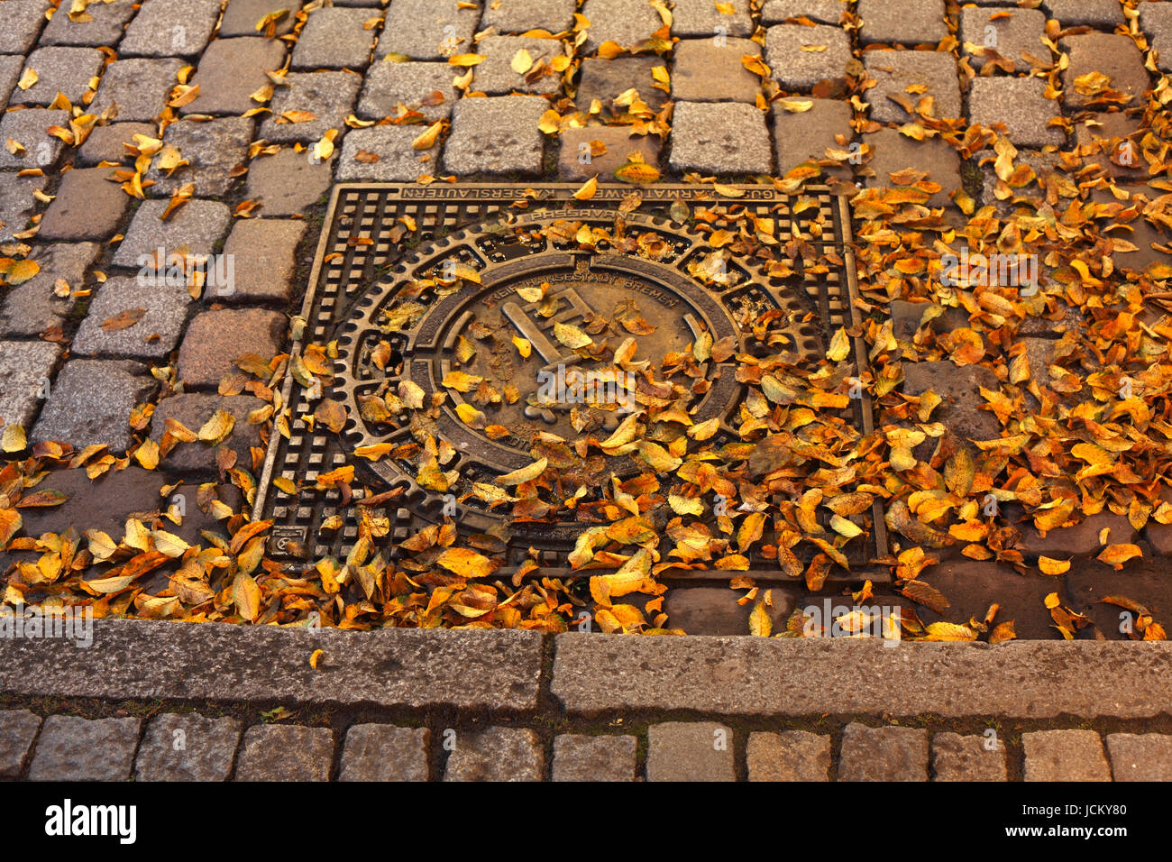 Bremer Schluessel auf Kanaldeckel mit gelben Herbstlaub und Bordstein, Bremen, Germany     I  Coat of arms on a Iron Manhole Cocer,Bremen key on canal Stock Photo