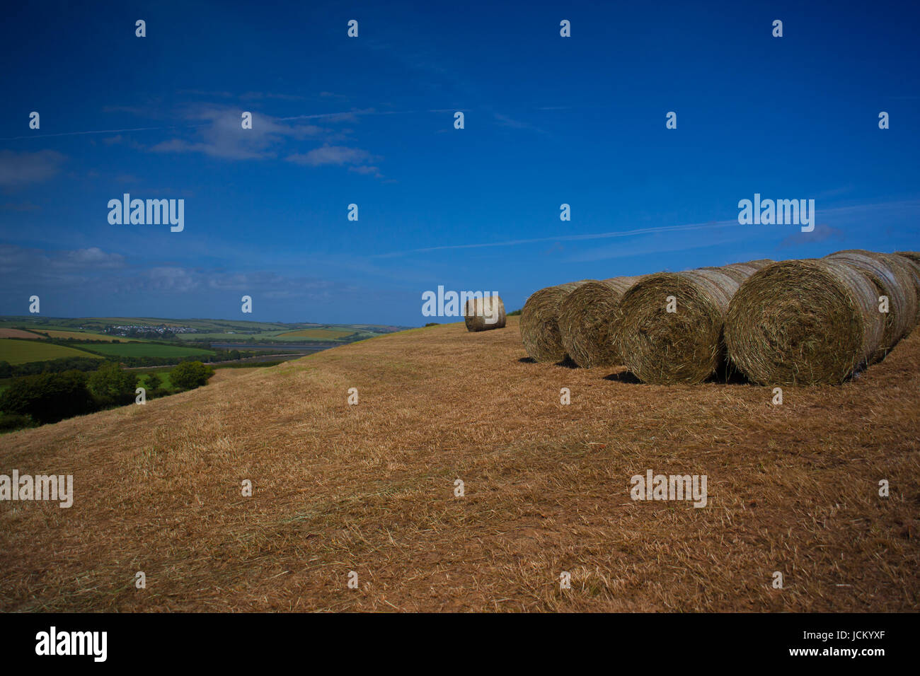 Straw bales perched on a rolling hillside with view across the valley Stock Photo