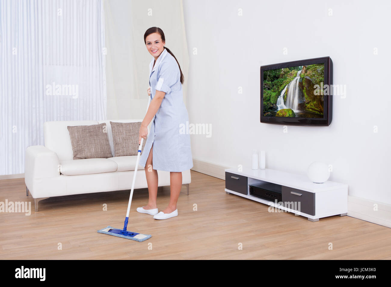 Full length portrait of young maid cleaning floor with mop at home ...