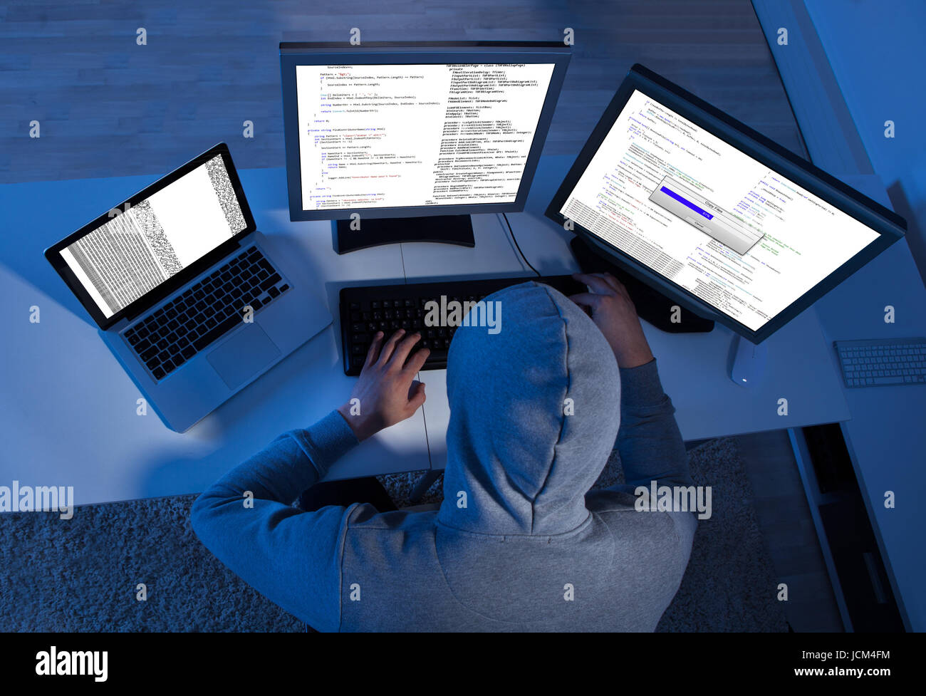 Side view of hacker using multiple computers to steal data at table ...