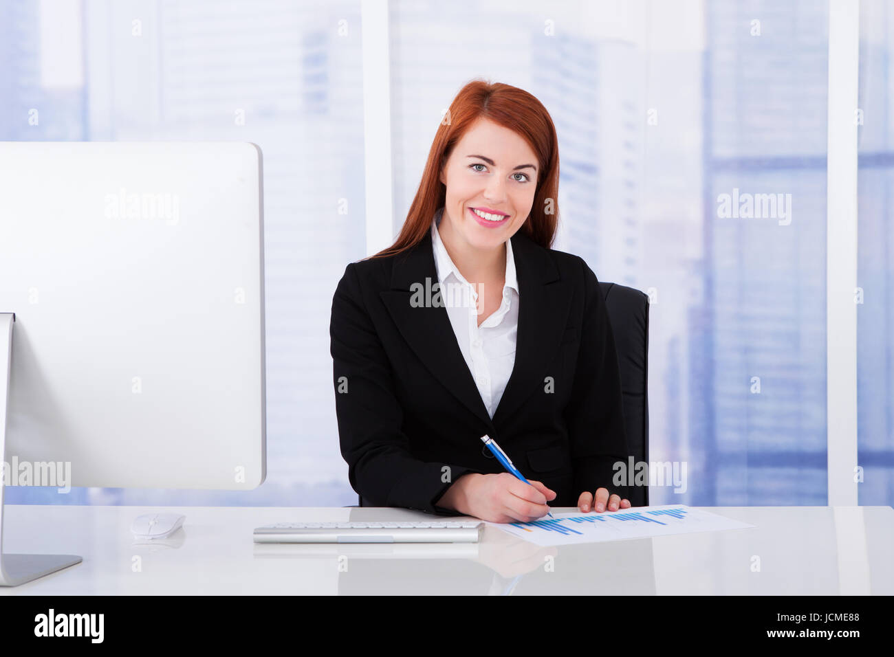 Happy young businesswoman using computer at office desk Stock Photo - Alamy