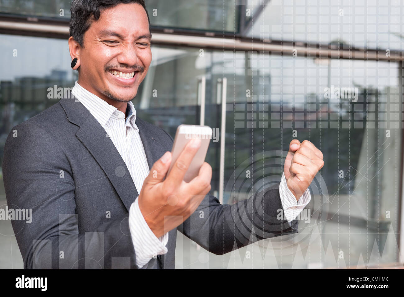 Successful asian business man checking cellphone message and gesturing with happiness and gladness outside office building. Start up entrepreneur enjo Stock Photo