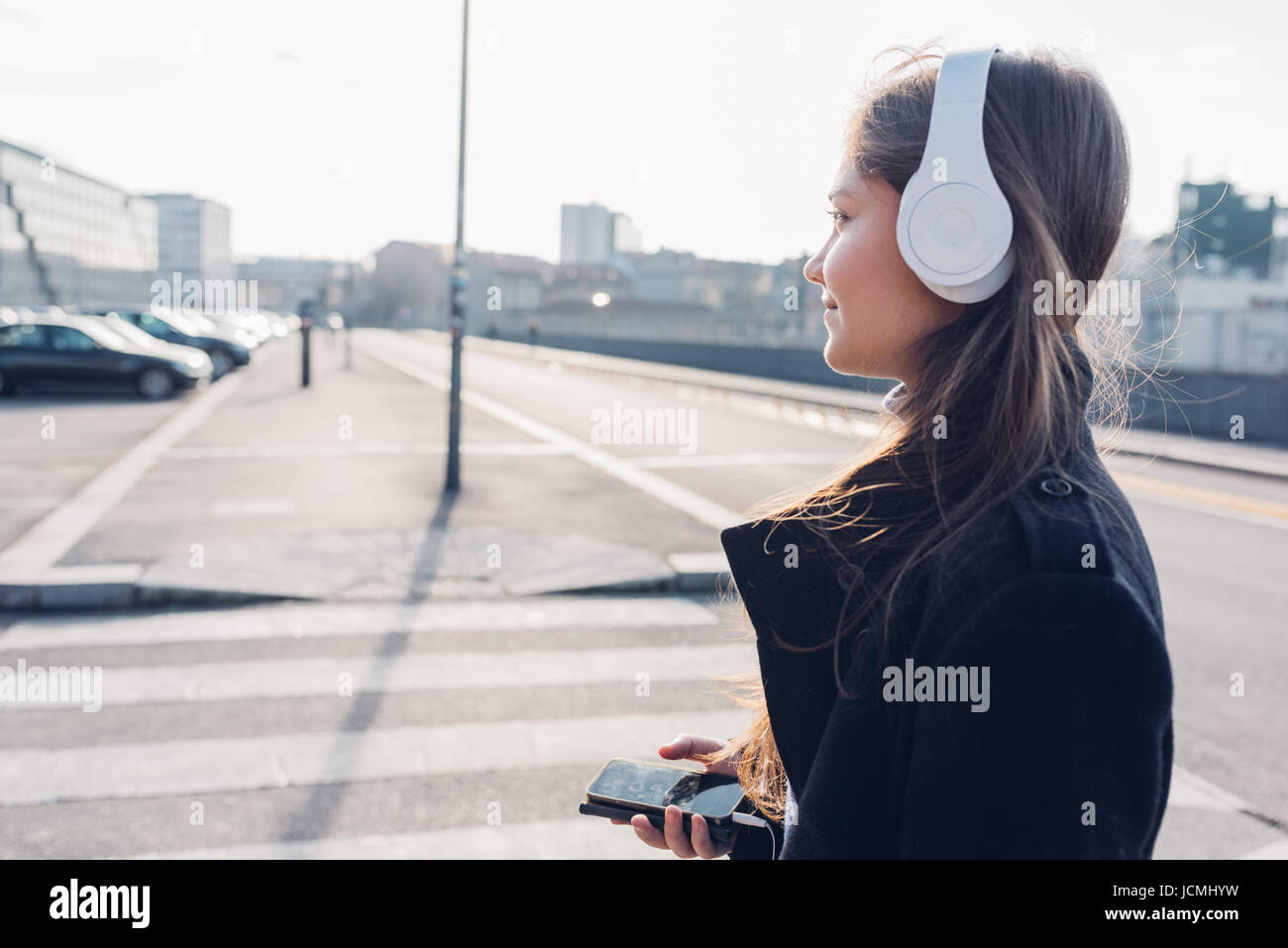 Side view young woman walking in the city back light listening music