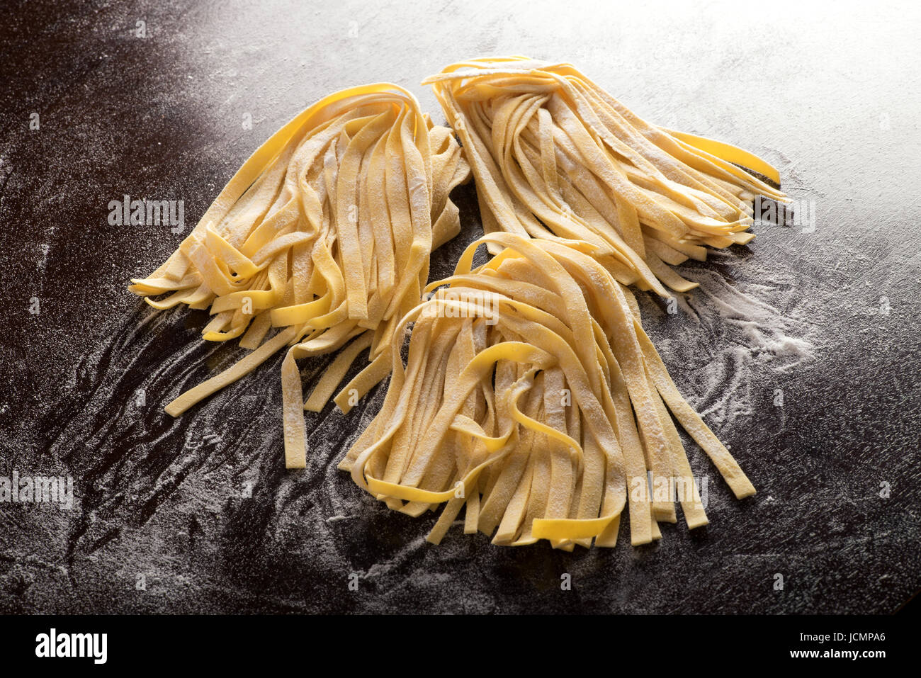Uncooked handmade Italian tagliatelle noodles on brown surface with