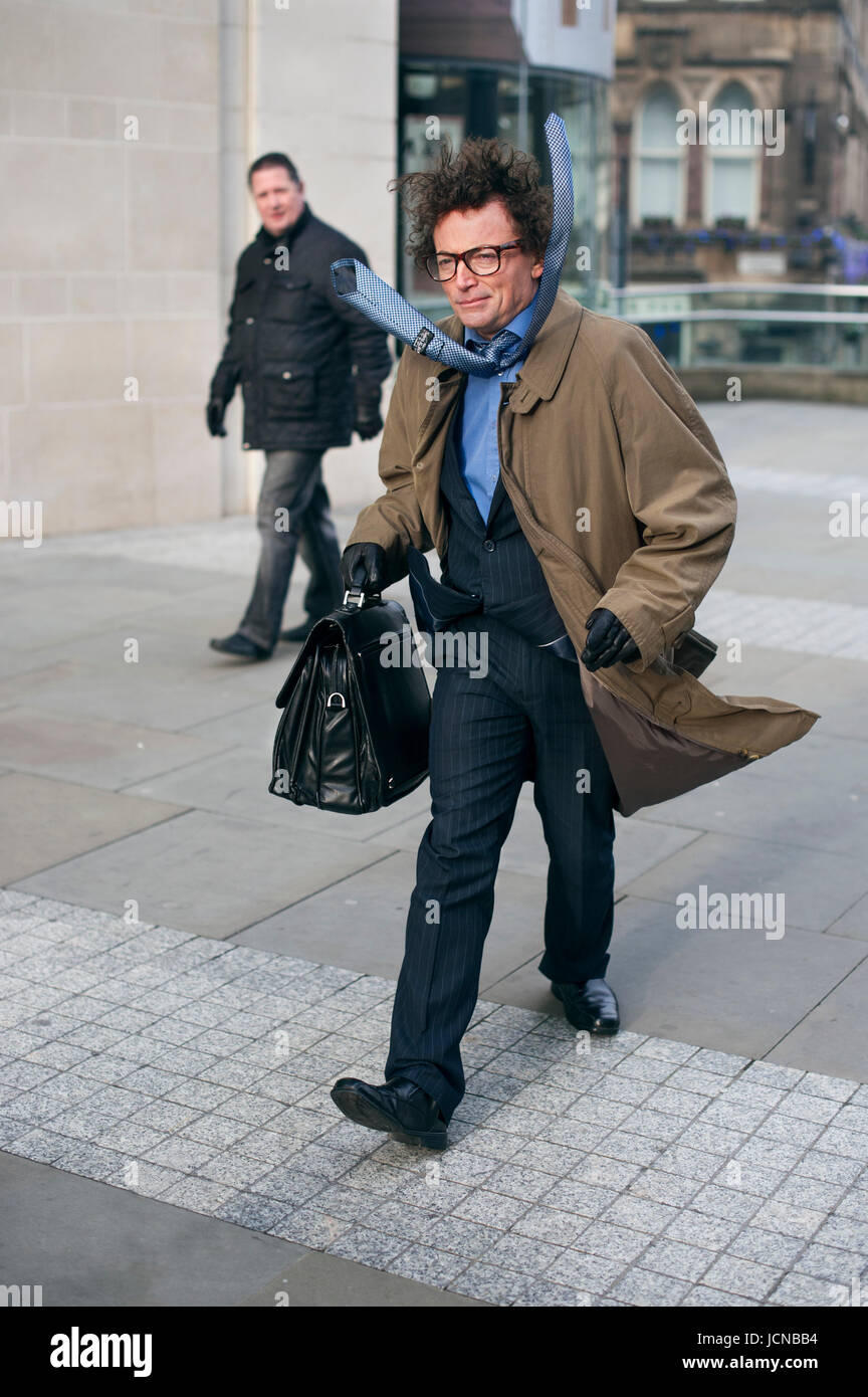 Wind blows man's coat and tie whilst he rushes through Manchester Stock Photo